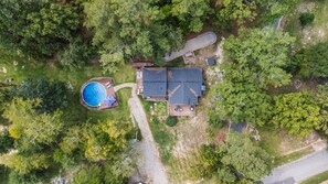 Vue aérienne d’une maison dotée d’une piscine, d’une terrasse et d’un grand jardin entouré d’arbres.