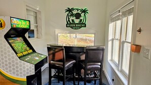 Ein Zimmer mit einem 3D-Golf-Arcade-Spiel, einem Tisch mit vier Stühlen und dem an der Wand befestigten Logo von Hamm House.