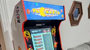 Ein Pac-Man-Spielautomat mit farbigem Design und einem Bildschirm, der Spieloptionen anzeigt.