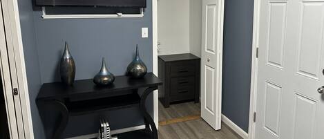 Una habitación con un televisor montado mostrando una pantalla de selección de perfil, un aparador negro con jarrones decorativos y una puerta blanca.