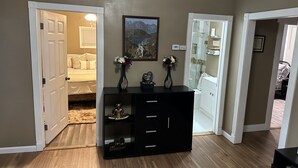 A hallway with a black console table, a framed picture of mountains, and a white door leading to a bedroom.