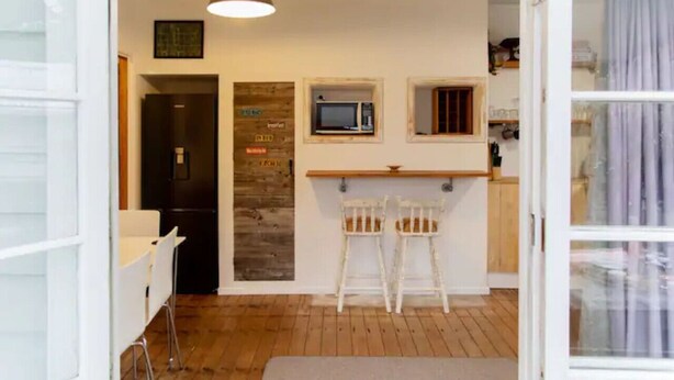A compact kitchen with a microwave, two stools, and a wooden accent wall. - Cosy Character Cottage in the City | Walk, Ride & Unwind (Rotorua)