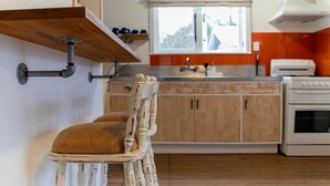 A kitchen with wooden cabinets, a white stove, and a window with a view of greenery. - Cosy Character Cottage in the City | Walk, Ride & Unwind (Rotorua)