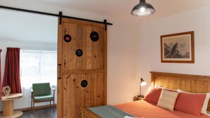 A bedroom with a wooden bed, a green chair, a wooden wardrobe, and a painting on the wall. - Cosy Character Cottage in the City | Walk, Ride & Unwind (Rotorua)