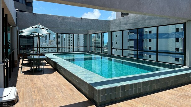 A rooftop pool area with a clear view of the cityscape, modern architecture, and a seating area with umbrellas. - APARTAMENTO ALTO LUXO (Recife)
