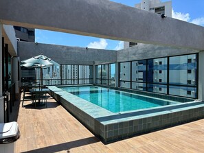 A rooftop pool area with a clear view of the cityscape, modern architecture, and a seating area with umbrellas. - APARTAMENTO ALTO LUXO (Recife)