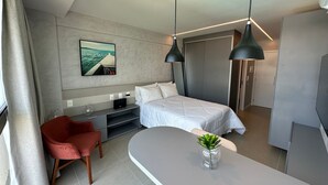 A modern hotel room with a bed, a desk, a chair, a small plant, and a painting on the wall. - APARTAMENTO ALTO LUXO (Recife)