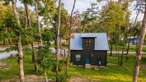 A small, dark-colored cabin surrounded by trees and a grassy area. - Sparks Fly / The Retreat at Water's Edge / 2 Kayaks, 1 Canoe, 1 Paddle Board (Tracy City)