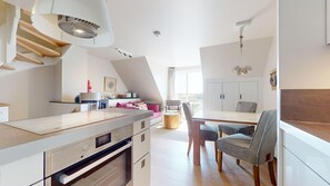 Una cocina moderna con horno empotrado, un comedor con mesa y sillas, y una escalera de madera.