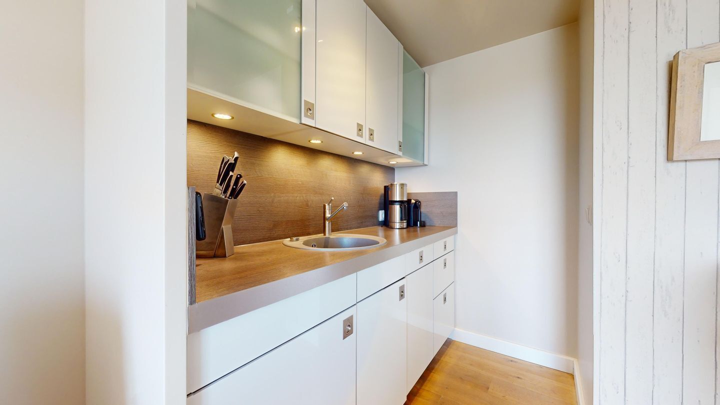 Eine moderne Küche mit weißen Schränken, einer Holz Arbeitsplatte und einem Edelstahlspülbecken.