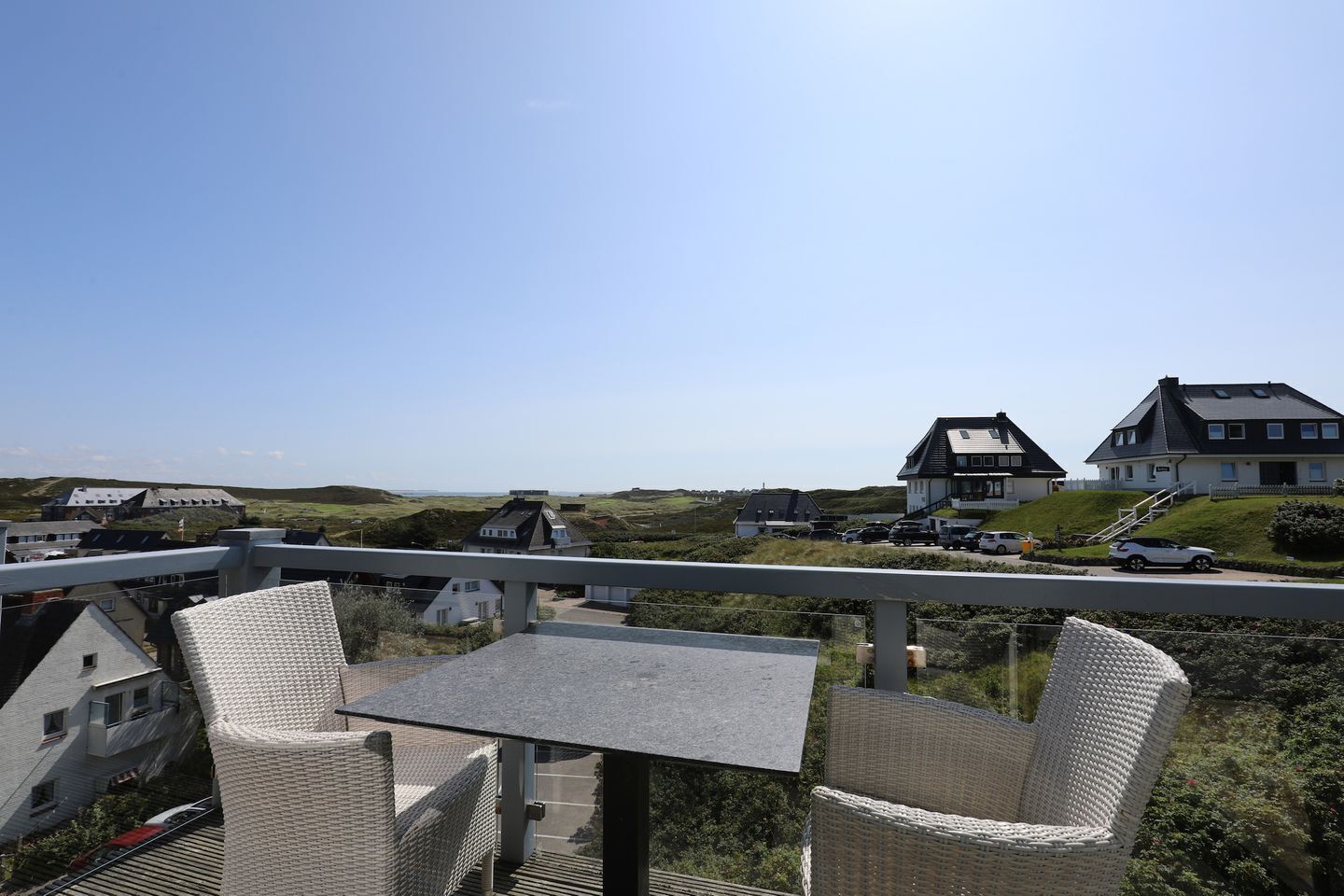 Ein Balkon mit Korbstühlen und einem Tisch mit Blick auf ein Wohngebiet mit Häusern und einer Bahnlinie.