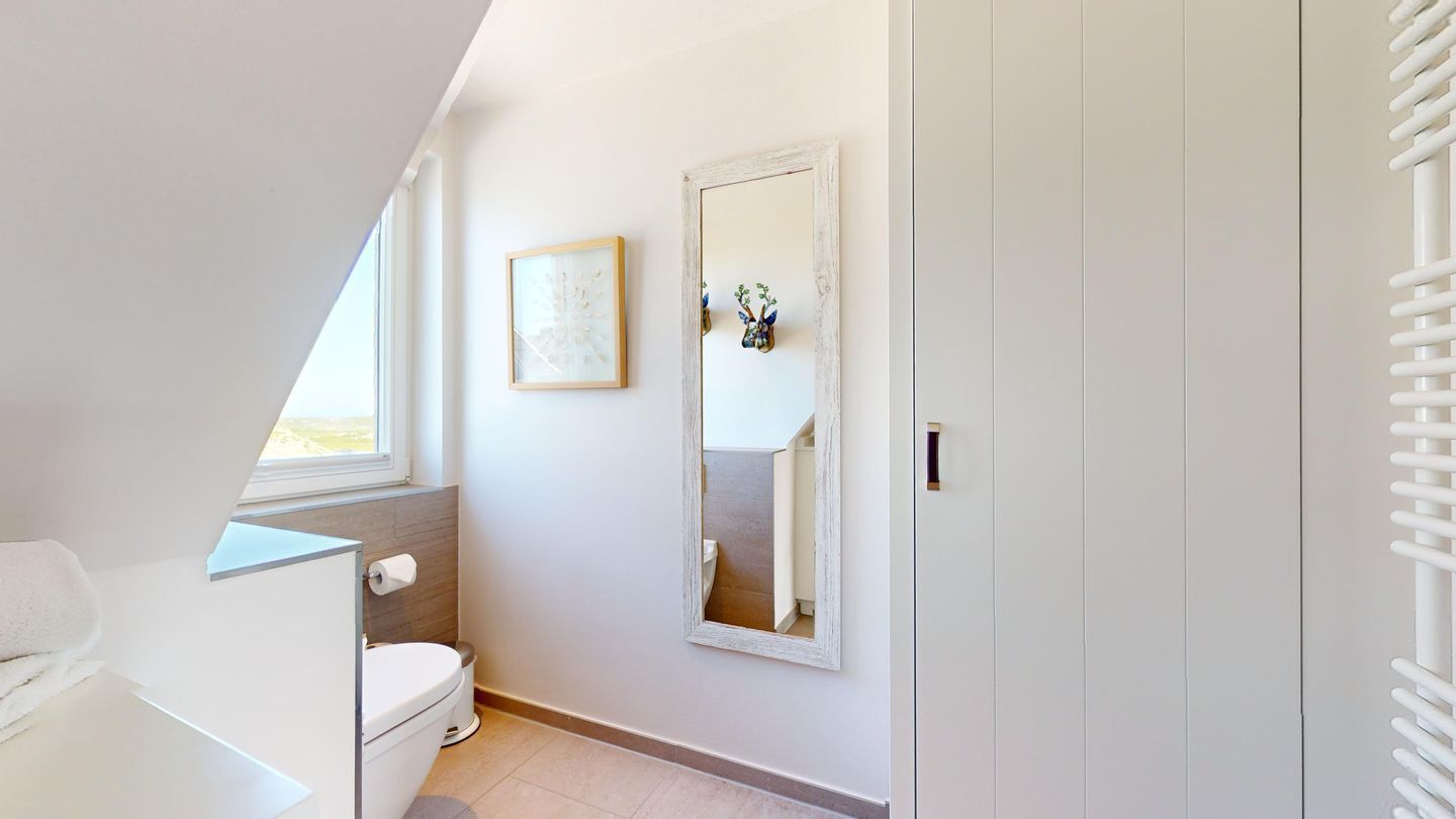 Une petite salle de bain blanche, équipée de toilettes, d’un porte-serviettes et d’un miroir.