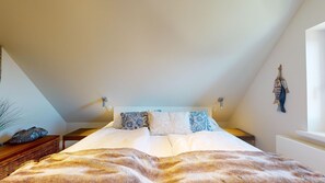 A bedroom with a bed, pillows, a bedside table, a lamp, and a wall decoration.