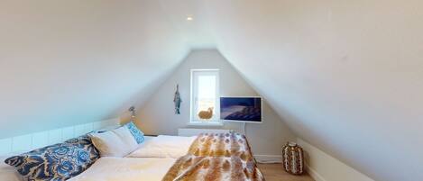 A bedroom with a sloped ceiling, a bed with patterned pillows, a television on a stand, and a small decorative item on the floor.