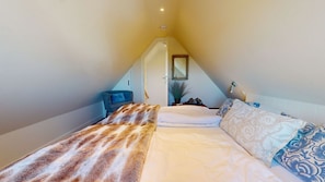 Une chambre avec un plafond en pente, un lit recouvert d’une literie à motifs, une petite table de chevet et un miroir au mur.