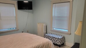 Une chambre à coucher comprenant un lit, une table de chevet, une lampe, un radiateur et un téléviseur fixé au mur.