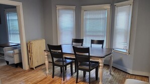Un espace repas avec un plancher en bois, une table entourée de quatre chaises et un luminaire au plafond.