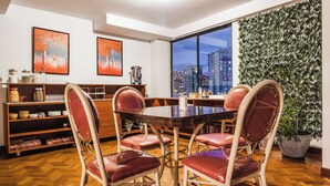 Un comedor con una mesa de madera y cuatro sillas, un ventanal con vista a la ciudad y una pared cubierta de follaje verde.