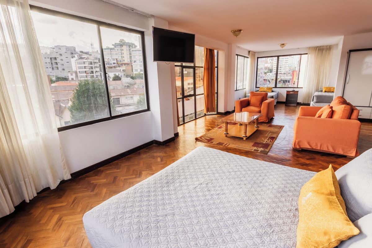 A spacious living room with a large window, a flat-screen TV, orange sofas, and a wooden floor.