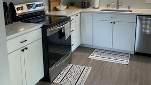 Una cocina moderna con armarios blancos, estufa de acero inoxidable, microondas y horno empotrado. Hay un ventanal sobre el fregadero y una ventana pequeña en la pared.