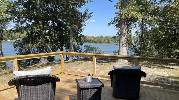 Una terraza de madera con mobiliario de mimbre y vistas a un lago.