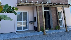 Een modern gebouw met twee verdiepingen, grote ramen, een houten pergola en het cijfer '75' is duidelijk zichtbaar.