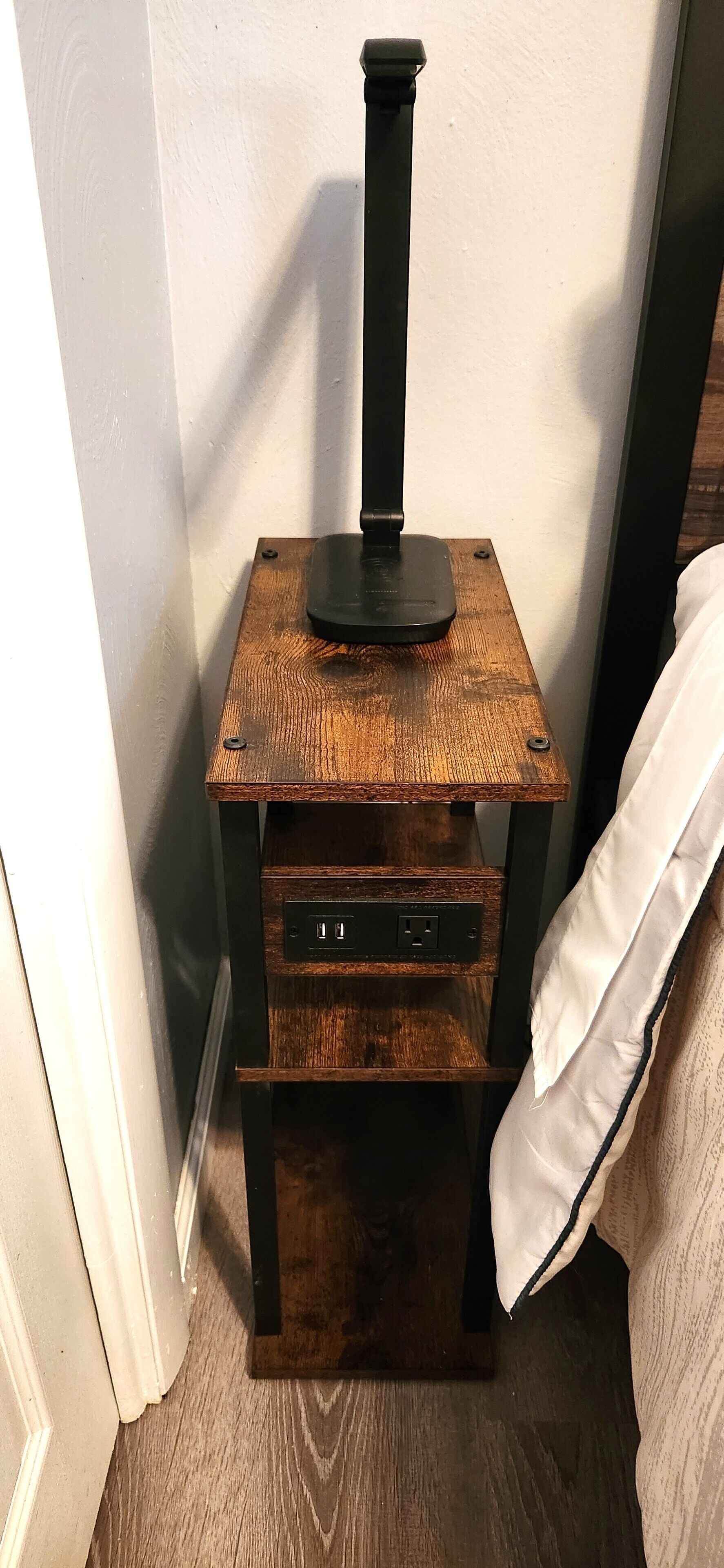 Un tavolo d'angolo con base nera e piano in legno, dotato di una presa di corrente.