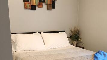 A neatly made bed with a dark-colored comforter and pillows, a wooden floor, and a wall-mounted artwork above the bed.