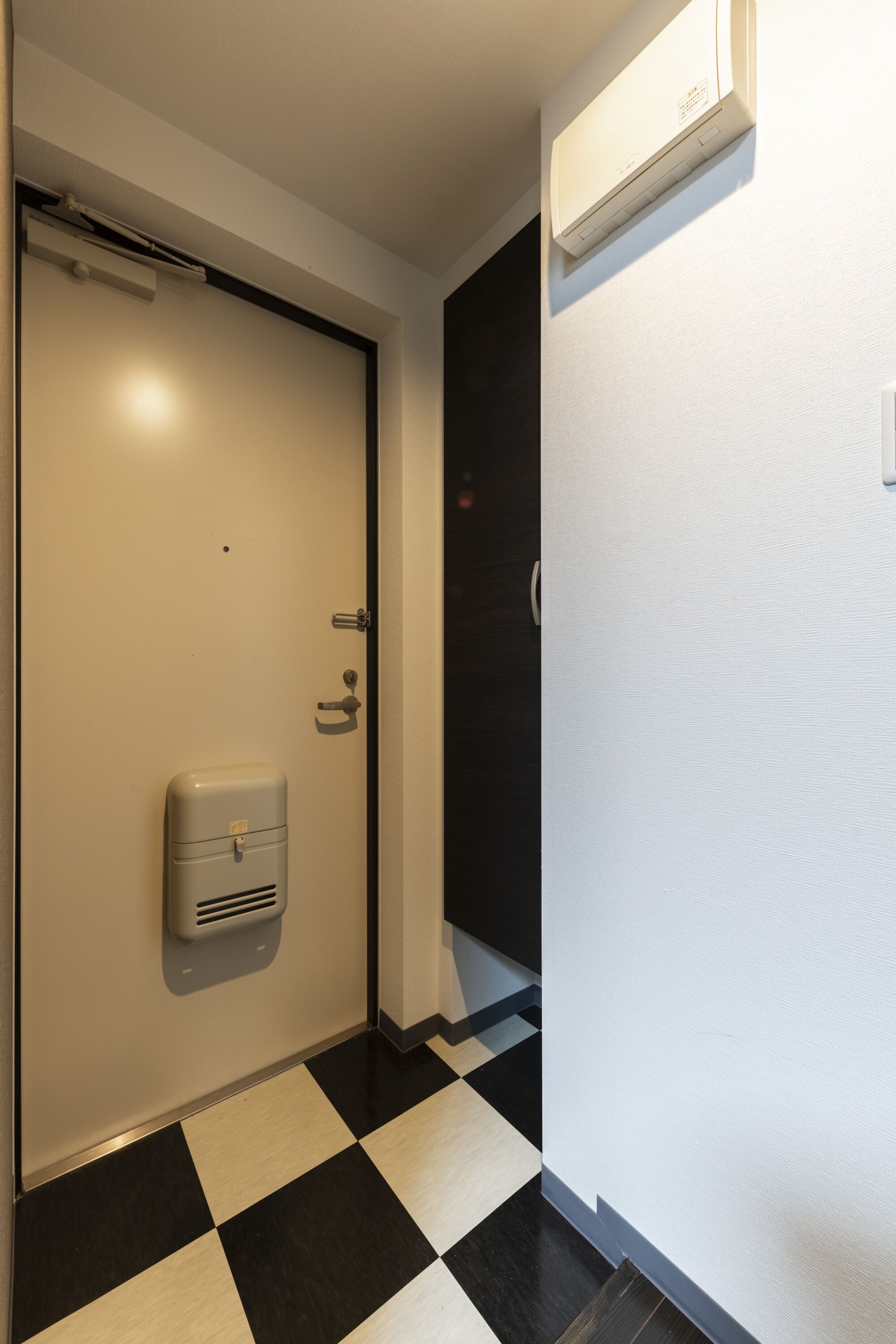 A hotel room with a checkered floor, a door with a handle, and a wall-mounted air conditioner.