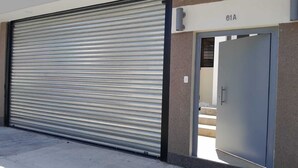 A closed metal garage door with a number "61A" above it, indicating a specific unit or location. - THE HEROES HOUSE (San Salvador)