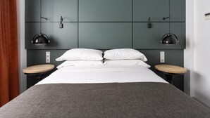 Ein modernes Hotelzimmer mit einem großen Bett, zwei Nachttischen und einem grünem Kopfteil mit Wandleuchten.