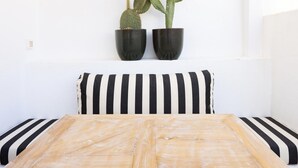 Ein Bett mit schwarz-weißen Kissen, zwei Zimmerkaktusse an einer weißen Wand und ein Holz-Kopfteil.