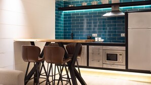 A modern kitchen with a blue backsplash, stainless steel appliances, and a wooden dining table with chairs. - Chayofa Suites - Deluxe (Santa Cruz de Tenerife)