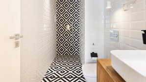 A modern bathroom with a geometric patterned shower wall, a white toilet, and a wooden vanity with a white sink. - Chayofa Suites - Deluxe (Santa Cruz de Tenerife)
