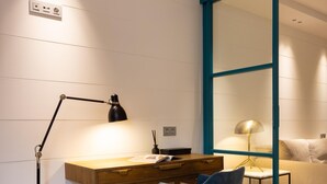 A modern room with a wooden desk, a blue chair, a glass partition, and a bed with a white headboard. - Chayofa Suites - Deluxe (Santa Cruz de Tenerife)