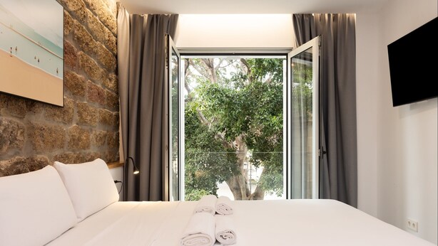 A hotel room with a large bed, a stone wall, a TV, and a view of trees through a glass door. - ★ New · Guimera Family Suites - A (Santa Cruz de Tenerife)