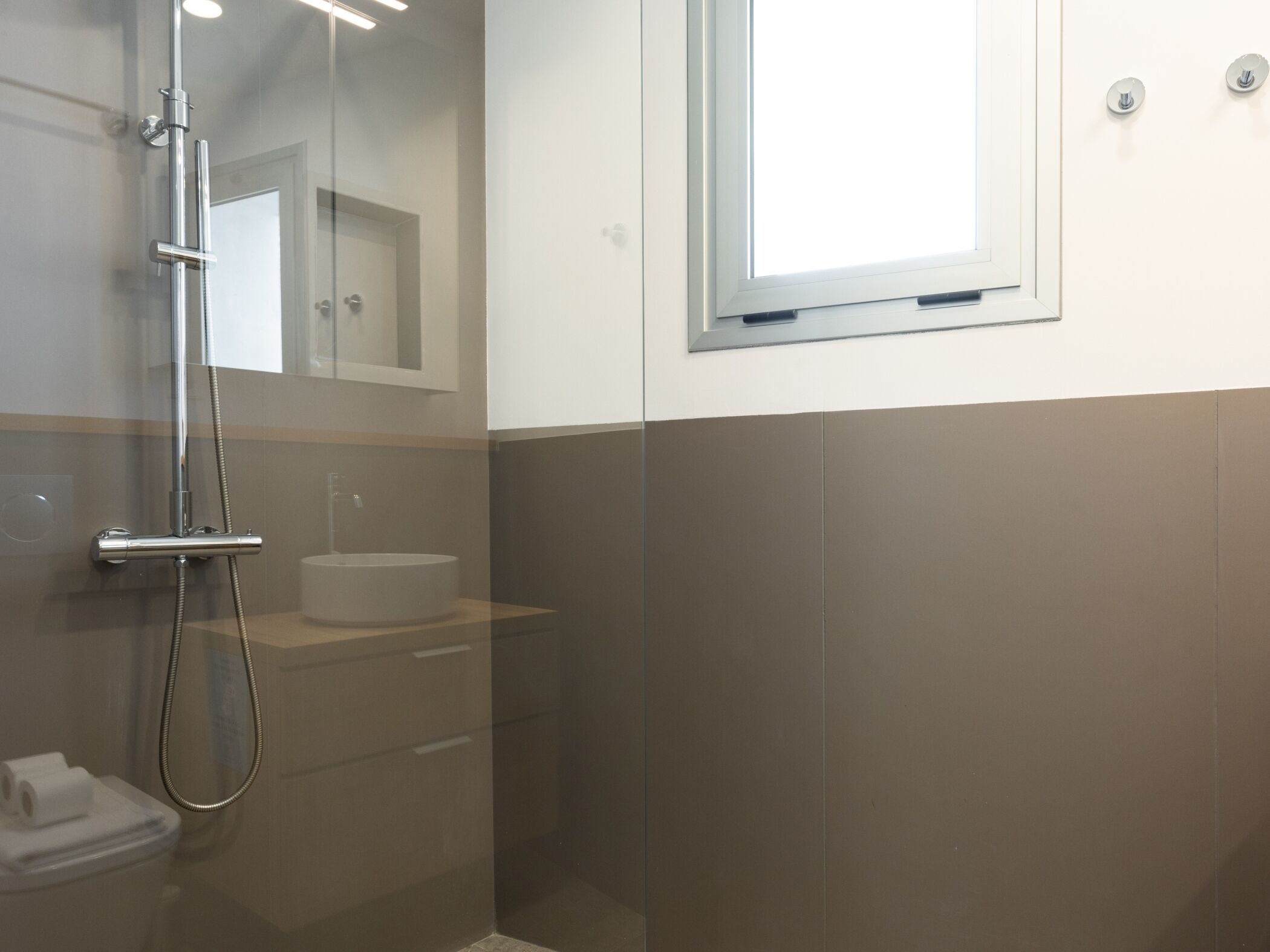 Ein modernes Badezimmer mit Duschkabine aus Glas, einem runden Waschbecken und einem Spiegel darüber.