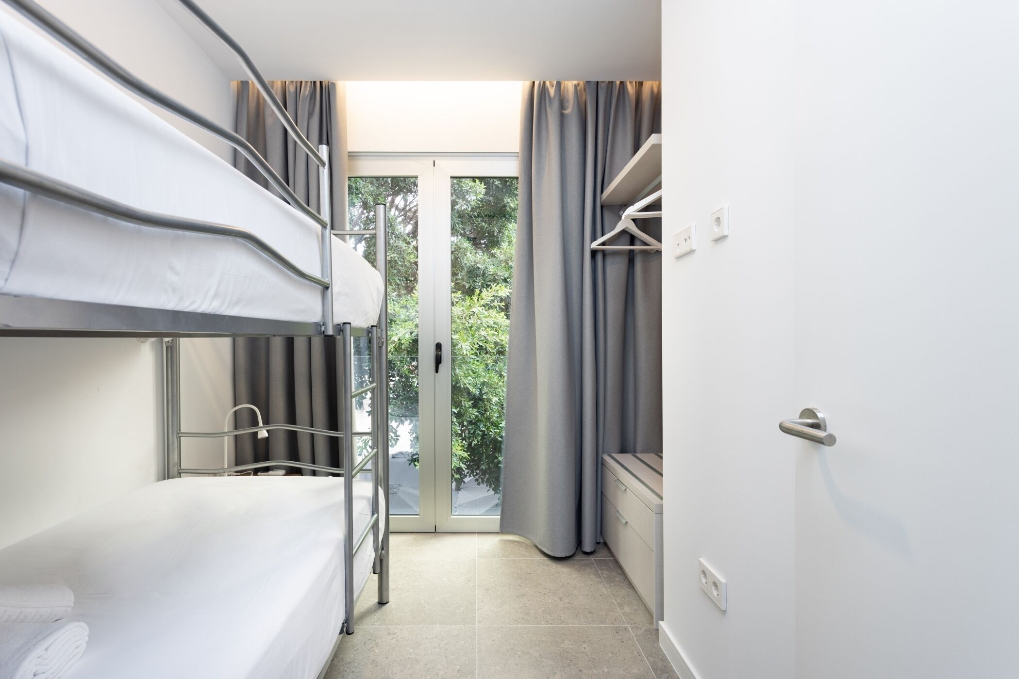 A compact hotel room with a bunk bed, a small seating area, and a sliding glass door leading to a balcony.