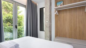 Ein modernes Hotelzimmer mit einem großen Bett, einer Wandpaneele aus Holz, einem Fenster mit Vorhängen und einem kleinen Regal mit einem Bild.
