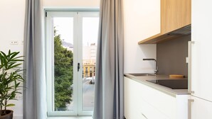 Eine moderne Küche mit einer Schiebeglastür, die auf einen Balkon führt, einer Topfpflanze und Blick auf Gebäude.