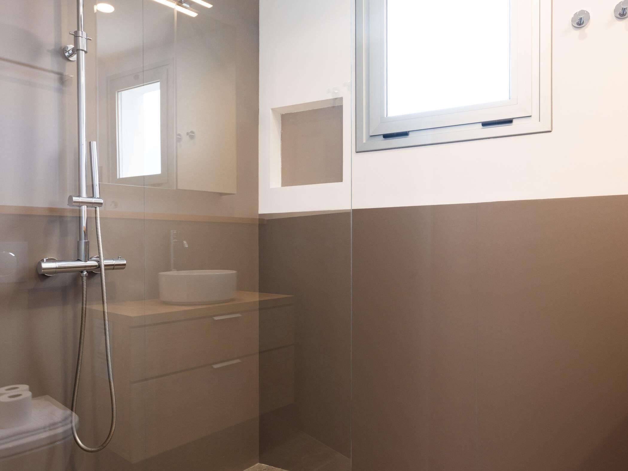 Ein modernes Badezimmer mit einer Duschkabine aus Glas, einem weißen Waschbecken und einem kleinen Fenster.