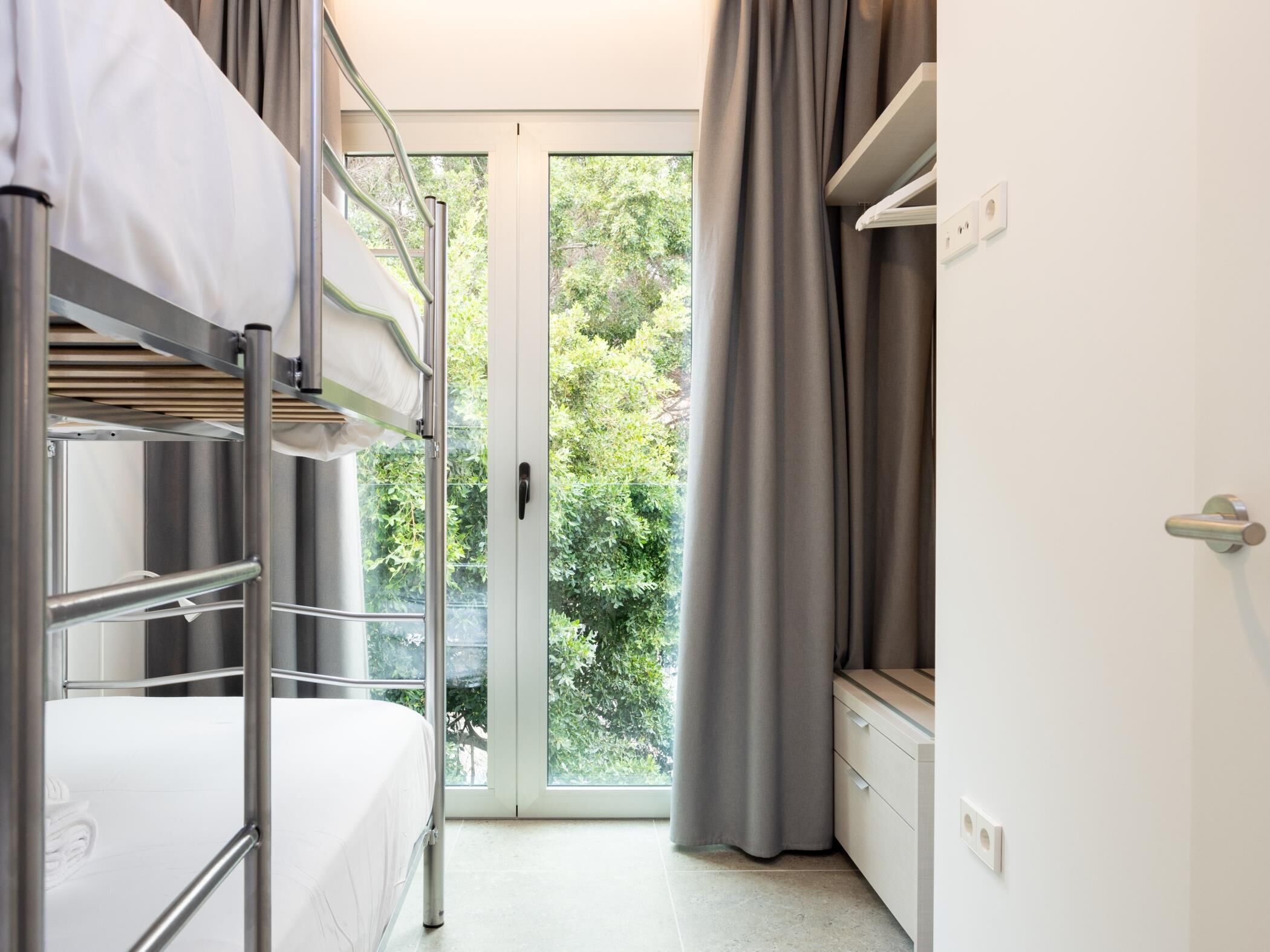 Une chambre avec des lits superposés, une porte-fenêtre coulissante donnant sur un balcon et un petit bureau avec des tiroirs.