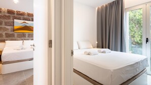 Ein modernes Schlafzimmer mit einem großen Bett, Blick auf Grün hinter einer Schiebeglastür und einer Ziegelwand mit einem Gemälde.