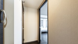 A hallway leading to a bedroom with a large window, a door with a handle, and a light switch on the wall. - Essence (Sapporo)