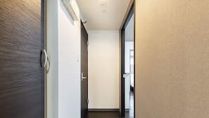 A hallway with a wooden door on the left, a white door in the center, and a beige wall on the right. - Essence (Sapporo)