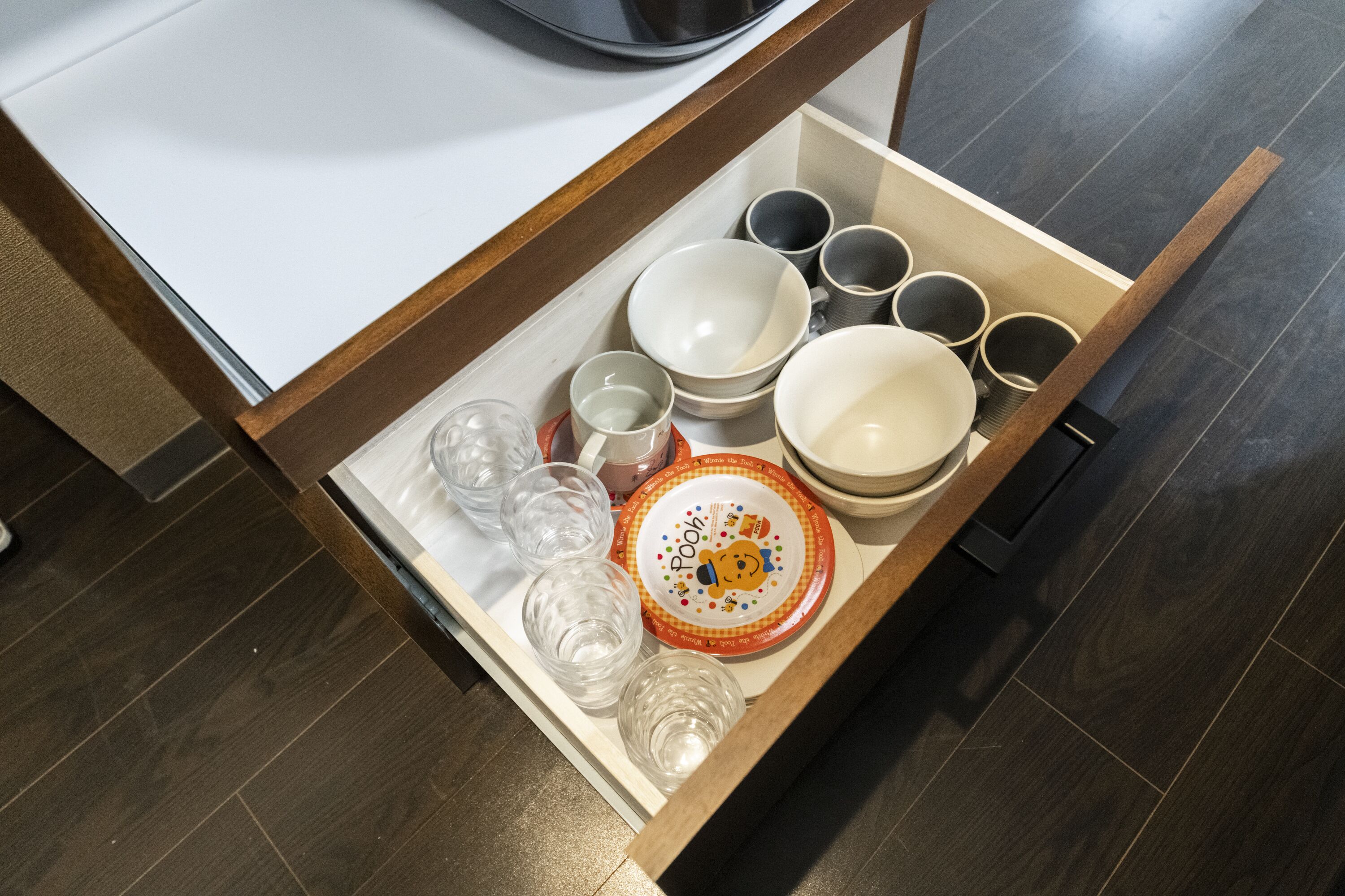 A drawer containing various kitchenware including bowls, cups, and glasses.