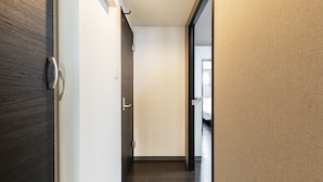 A modern hallway with a wooden floor, a door with a handle, and a view into a room with a bed. - Estrella (Sapporo)
