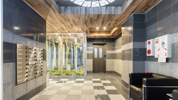 A modern lobby with a checkered floor, a glass wall with plants, a row of lockers, and a seating area. - Estrella (Sapporo)