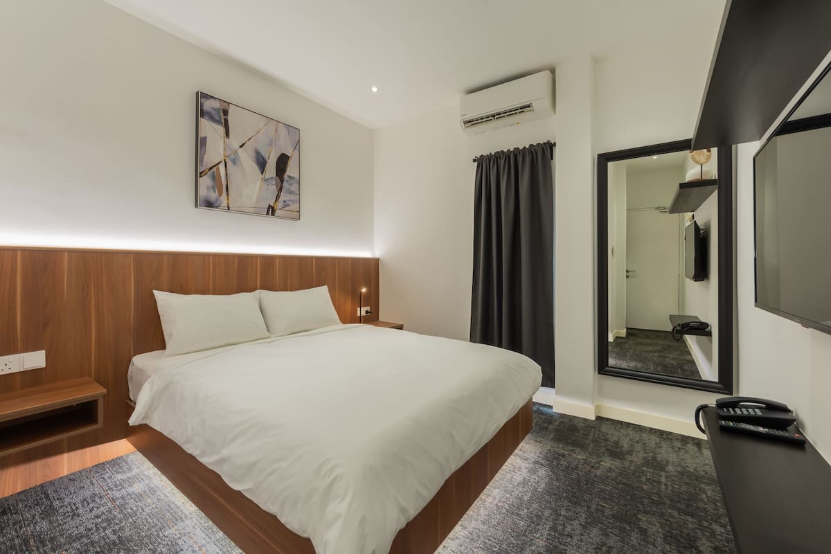 A modern hotel room with a large bed, a bedside table, a flat-screen TV, and a mirror.