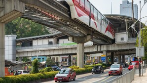 Un train circulant sur une voie surélevée, un immeuble à plusieurs étages avec une enseigne indiquant « Chow Kit », et divers véhicules dans la rue en contrebas.